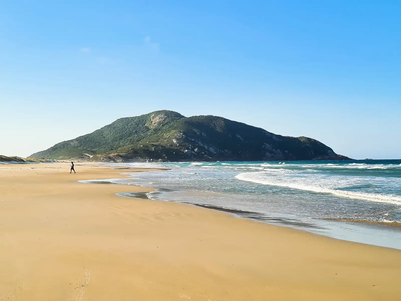 Praia de areia clara com um morro ao fundo, no sul de Florianópolis